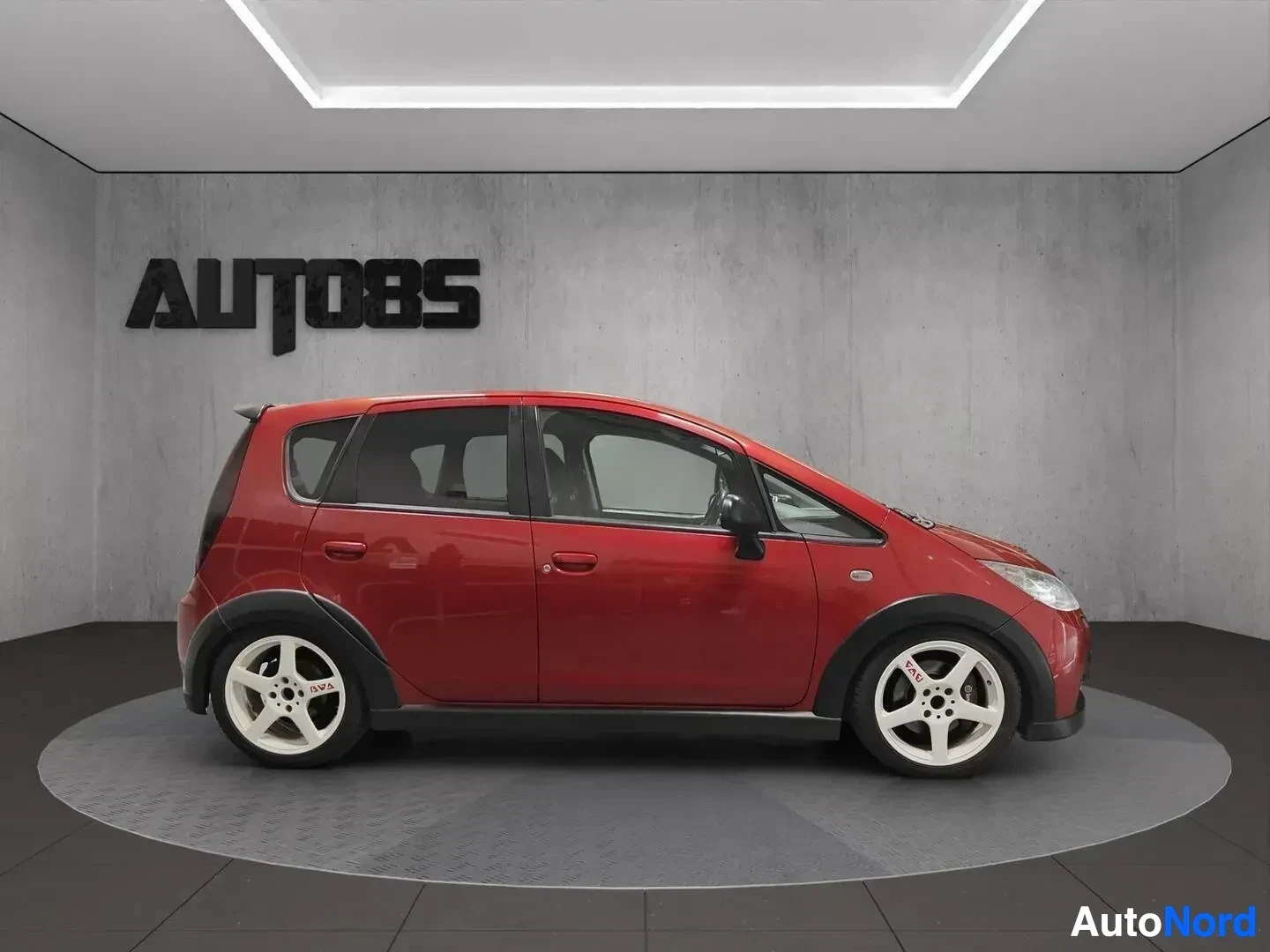 Sivulta: Punainen Mitsubishi Colt sivusta, valkokulmarenkaat, neljä ovea näkyvissä