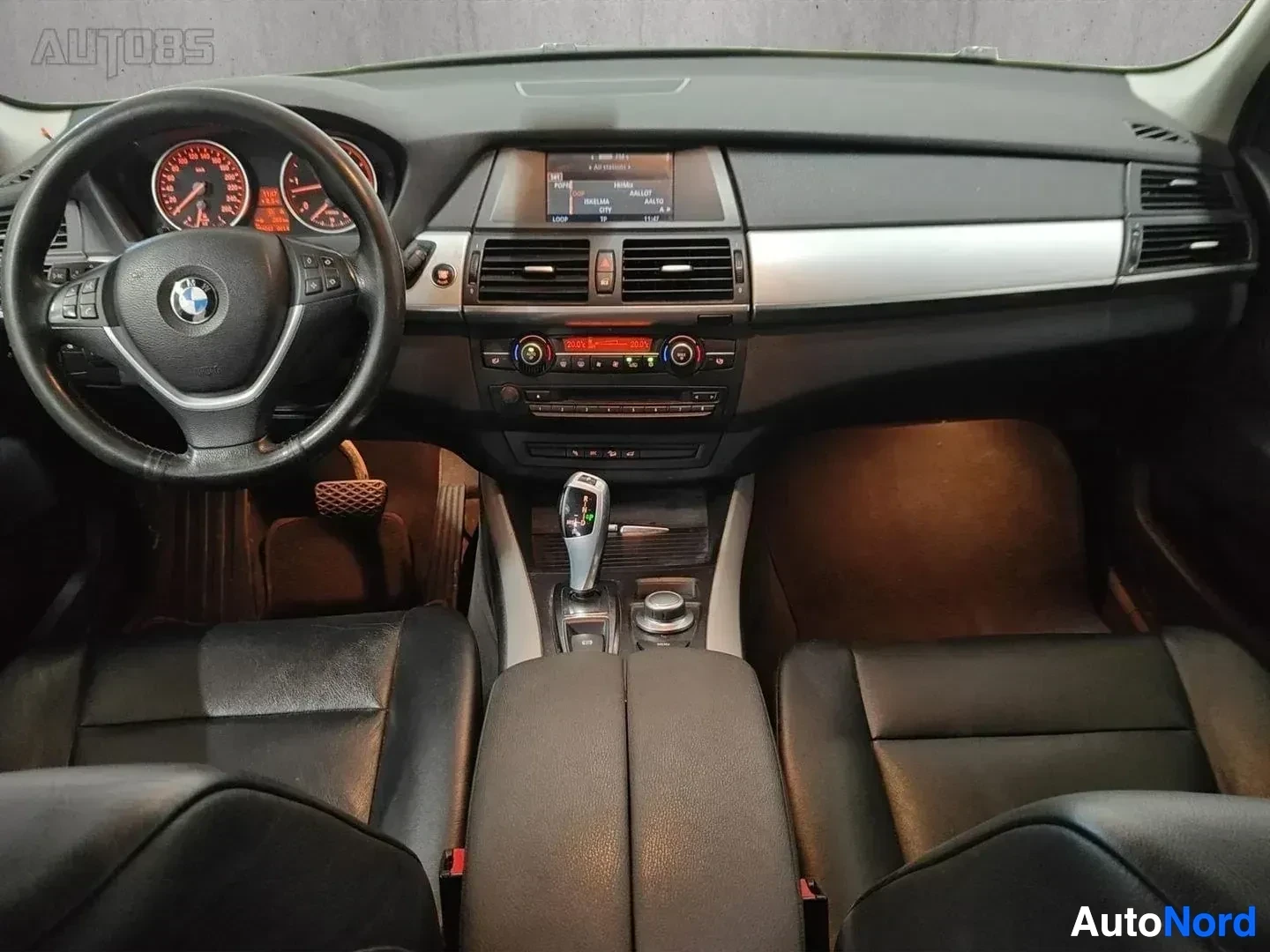 Ohjaamo: Auton kuljettajan paikka katsottuna kojelauta ja ohjauspyörä, BMW-logo, ruskeat ja mustat sisustukset, keskellä infotainment-näyttö