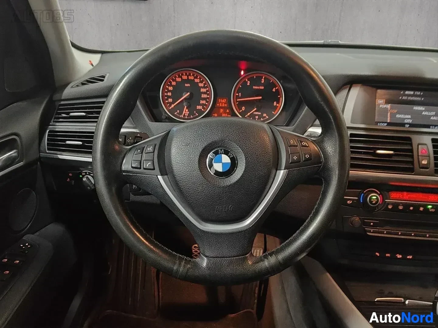 Yksityiskohta: Ohjauspyörä etulta, BMW-logo keskellä, punainen mittaristo, näyttö näkyy oikealla