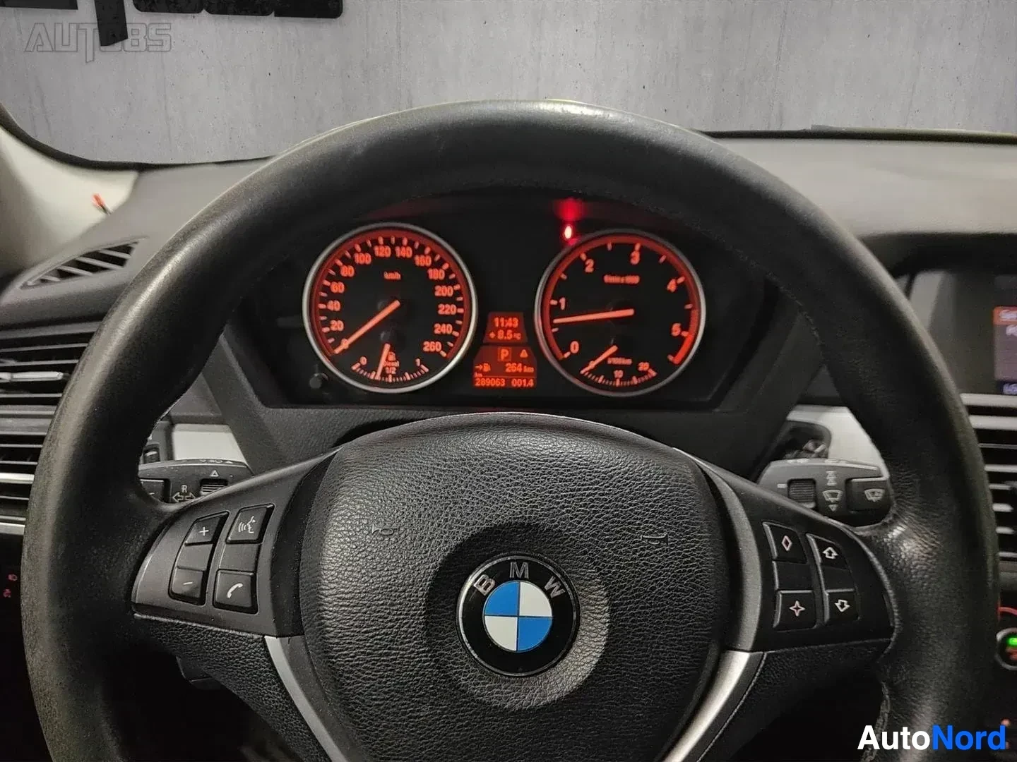 Yksityiskohta: Ohjauspyörä lähikuva, BMW-logo, punainen mittaristo näkyy ylhäällä, mustasta nahasta valmistettu