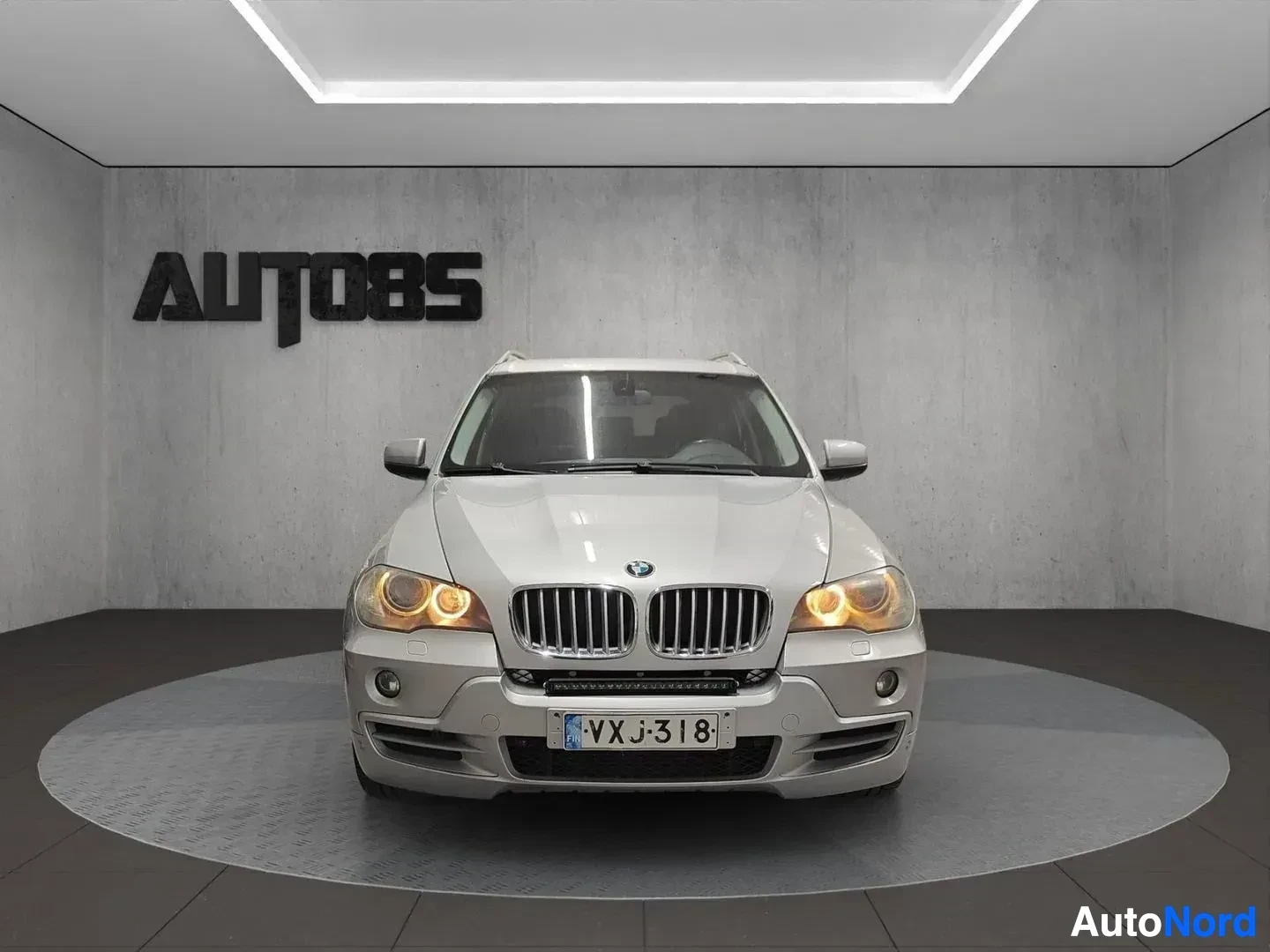 Edestä: Valkoinen BMW X5 -maasturi kuvattuna suoraan edestä sisätiloissa.