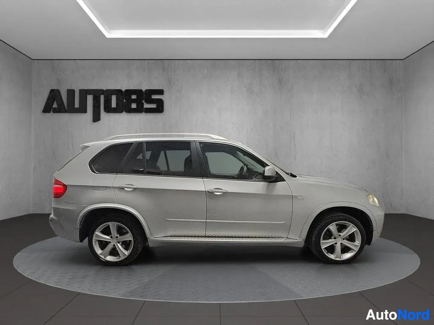 Sivulta: Hopeanvärinen BMW X5 -maastoauto sivusta kuvattuna vaaleassa studiossa. Auto on seisomassa harmaan lattialla