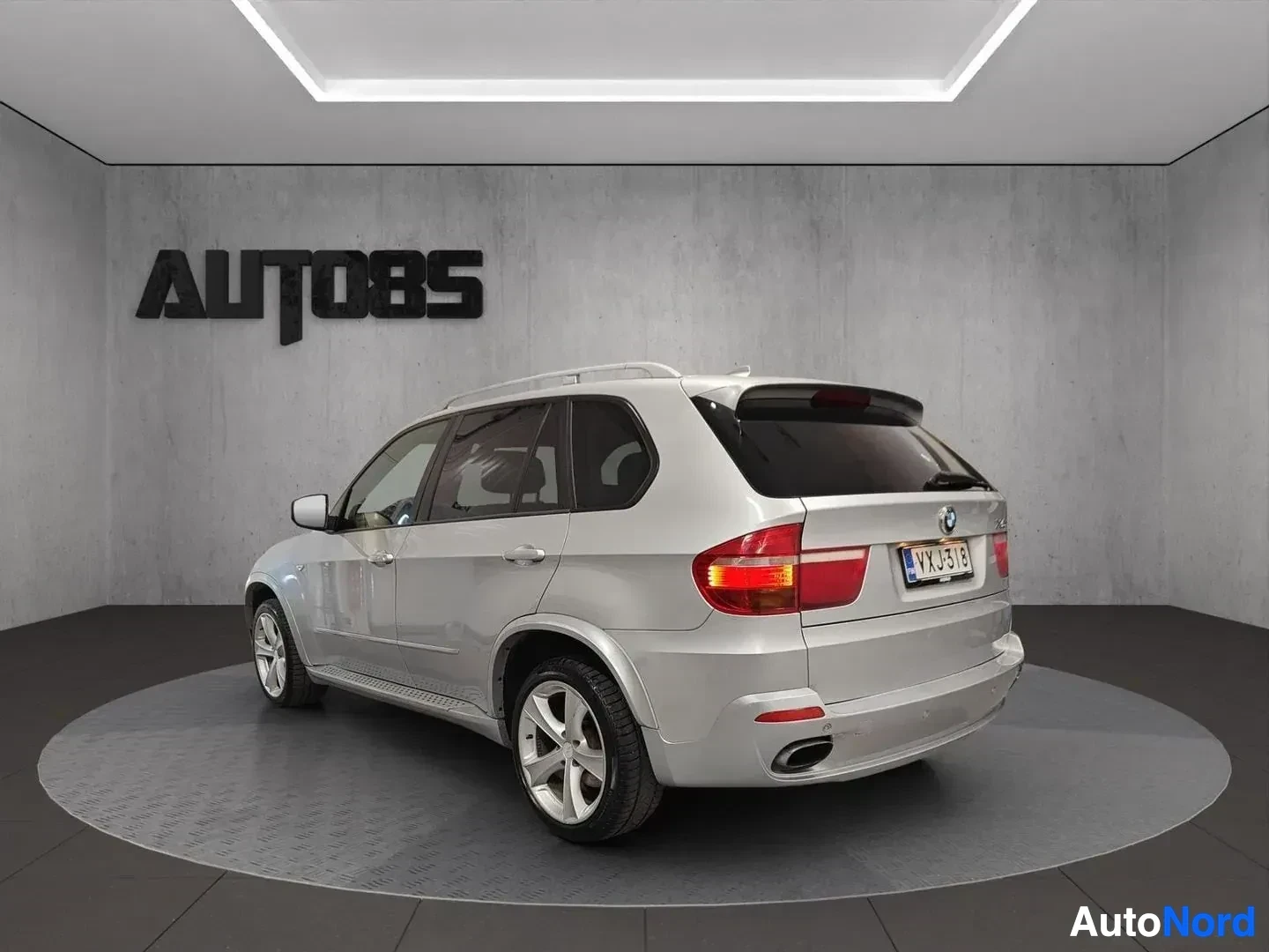 Takaviisto: Hopeanvärinen BMW X5 -maastoauto kolmen neljäsosan näkymästä kuin takaviistosta. Sivusta näkyy koko ajoneuvo. Auto seisoo studiossa.