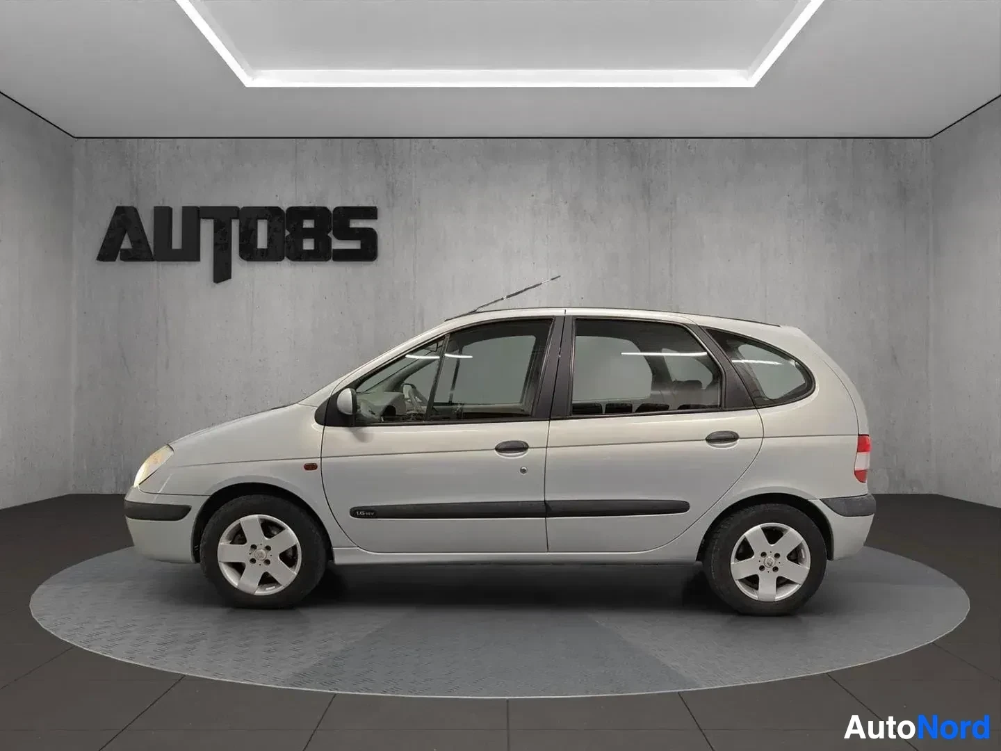 Sivulta: Valkoinen Renault Scenic -moniveto sivulta kuvattuna korkean katon alle asetetussa varastotilassa.