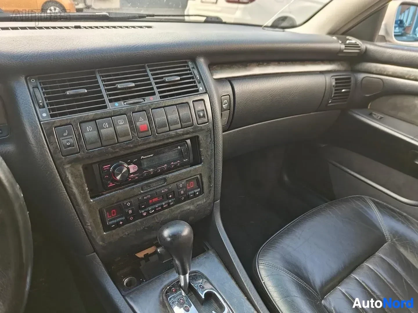 Yksityiskohta: Keskikonsoli ja ohjauspyörä. Pioneer-autostereo, ilmastoinnin painikkeet, mustat nahkaistuin oikella.