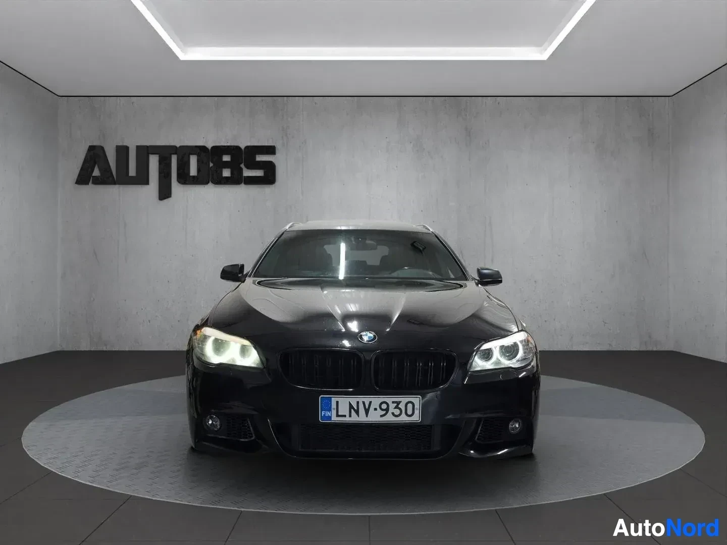 Edestä: Musta BMW-sedan etukuvan suorassa näkymässä, showroom-valaistussa tilassa