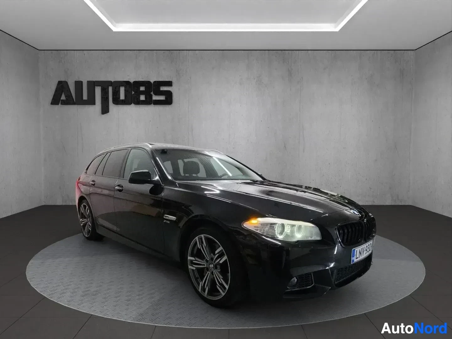 Etuviisto, nokka oikealle: Musta BMW-farmari, kolmen neljänneksen näkymä oikealta, valitut valaistut, showroom