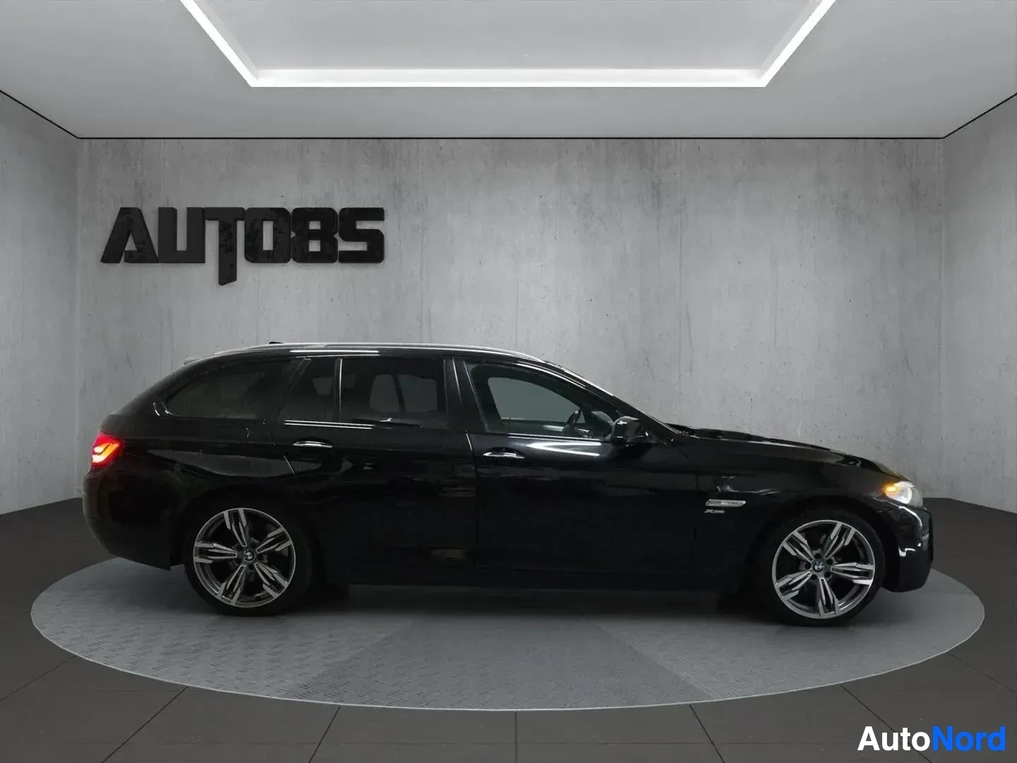 Sivulta: Musta BMW-farmari sivunäkymässä oikealta, valitut valaistut, showroom