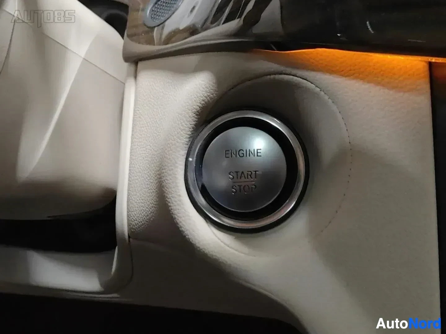 Yksityiskohta: Yksityiskohta moottorinkäynnistyksen painikkeesta beige värisellä ohjauspyörällä, tekstillä ENGINE START STOP.