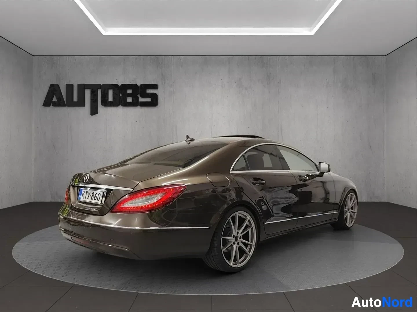 Takaviisto: Musta Mercedes-Benz CLS istuu kylpyhuonetyyppisessä showroom-tilassa, oikealle ja taaksepäin kääntyneenä, rekisterikilpi näkyvillä