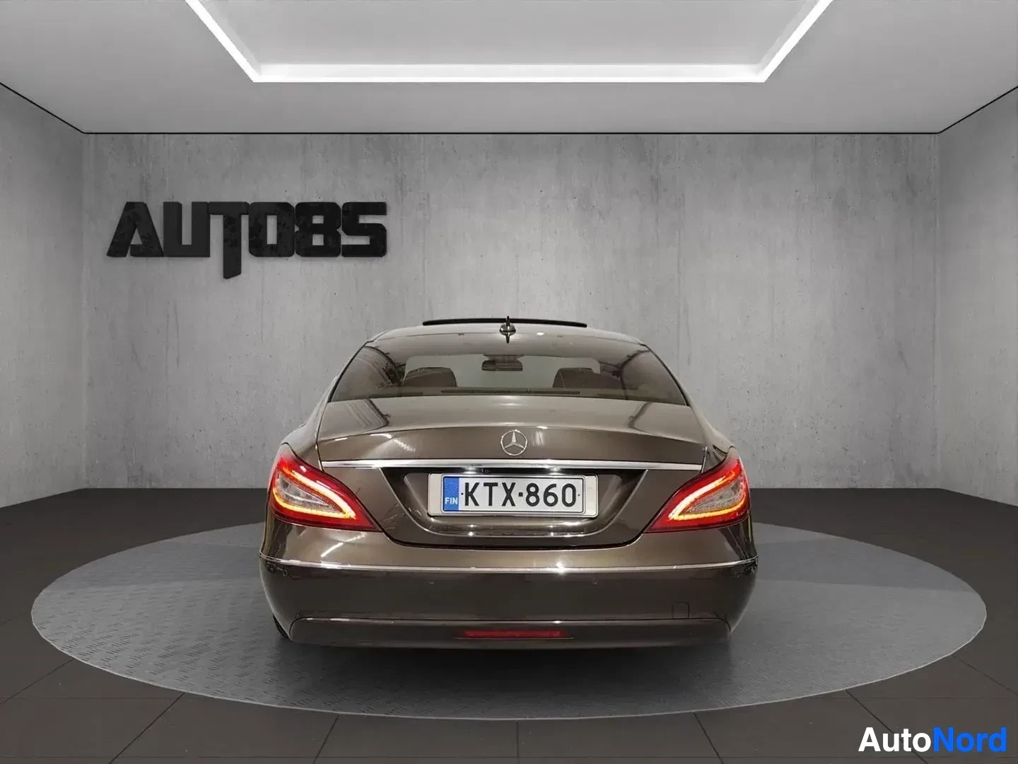 Takaa: Musta Mercedes-Benz CLS suoraan takaapäin kuvattu showroom-tilassa, rekisterikilpi näkyvillä, punaiset takavalot syttyneenä