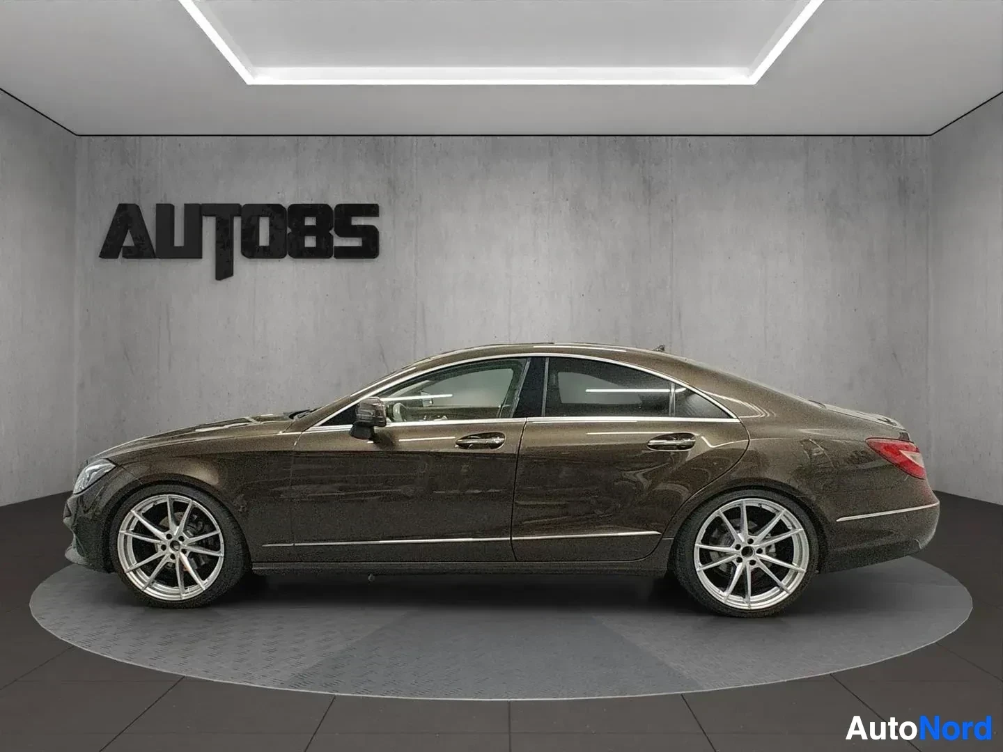 Sivulta: Musta Mercedes-Benz CLS suoraan sivulta kuvattu showroom-tilassa, neljä ovea näkyvillä, aluevanteet ja tummitetut ikkunat