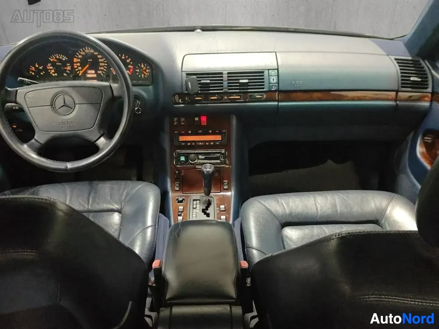 Ohjaamo: Auton sisätila etulta kuvattuna: nahkaverhoillut kuljettajan ja matkustajan istuimet, valkea kojelauta, puusta valmistettu sisustus, ratti Mercedes-Benz logolla