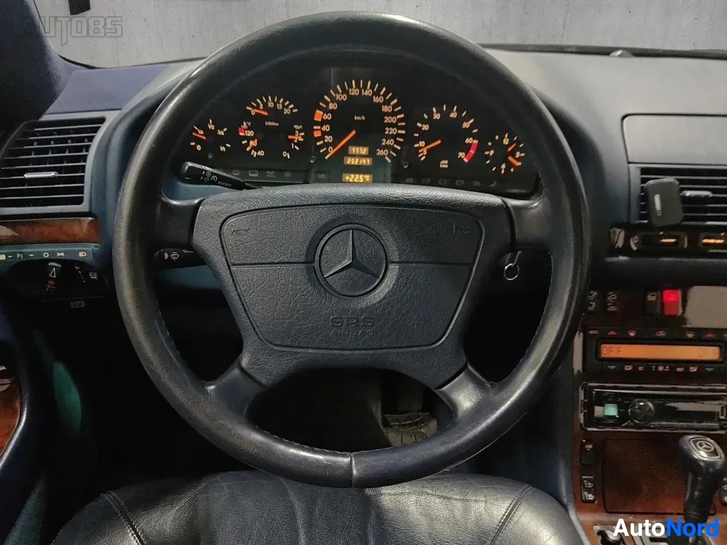 Yksityiskohta: Lähikuva rattista ja mittaristoista: Mercedes-Benz ratti, kunnostetut mittarit oranssein neuloin, nopeusmittari, kierroslukumittari ja muut ohjainvälineet.