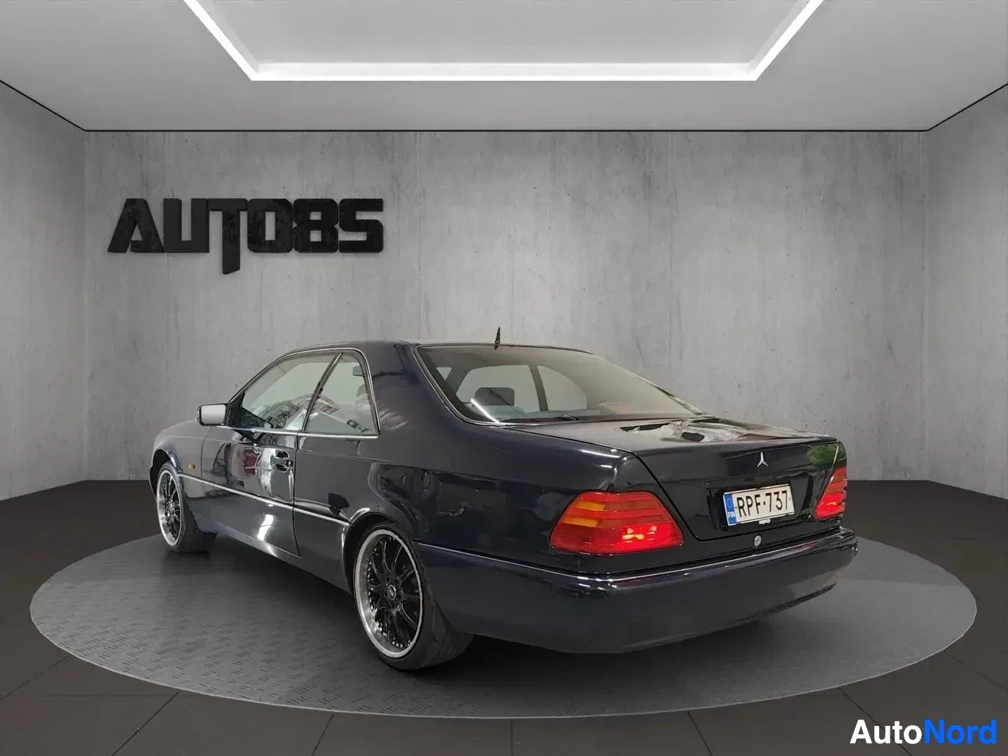 Takaviisto: Tummansininen Mercedes-Benz avointen ovien kanssa, kuvattu kolmesta neljäsosasta vasemmalta, rekisterikiilti RPF·73 osittain näkyvillä