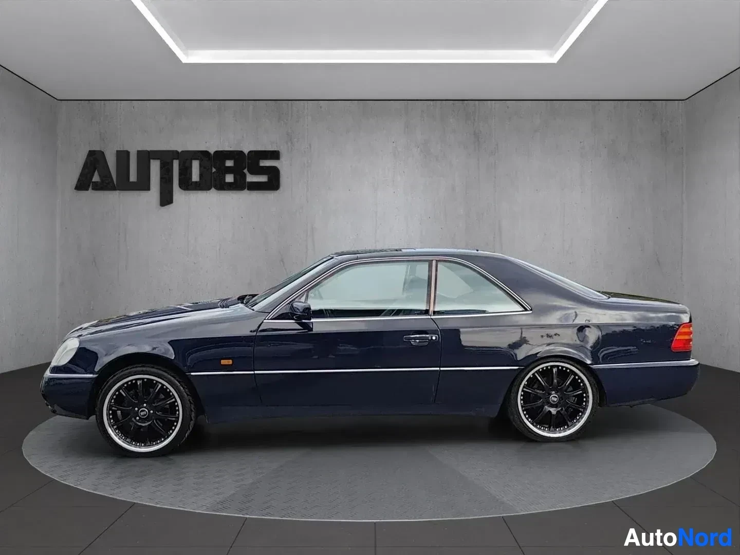 Sivulta: Tummansininen Mercedes-Benz C140 -coupe sivulta etukulmasta, mustat vanteet.