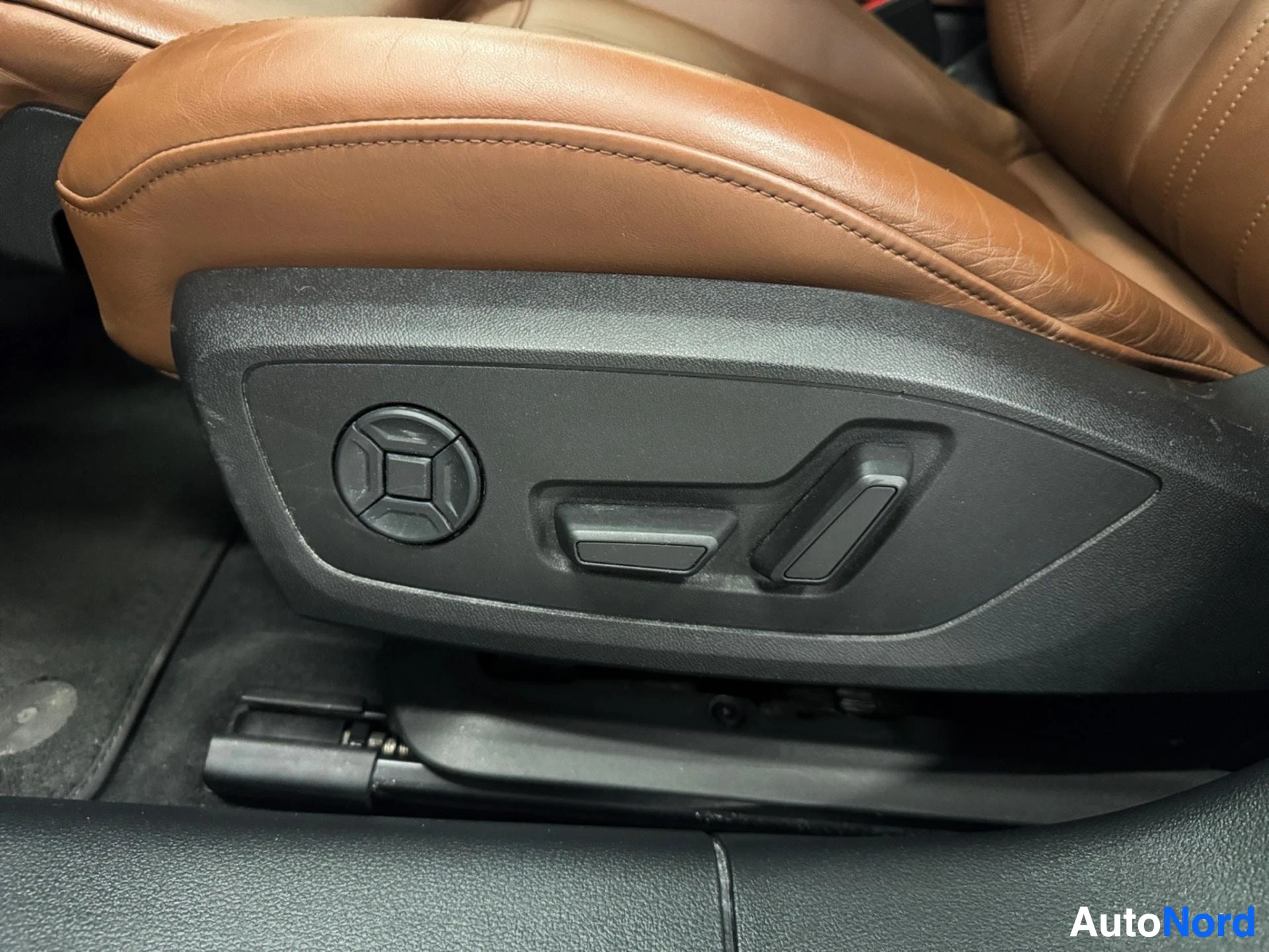 Close-up of brown leather driver seat with power adjustment controls