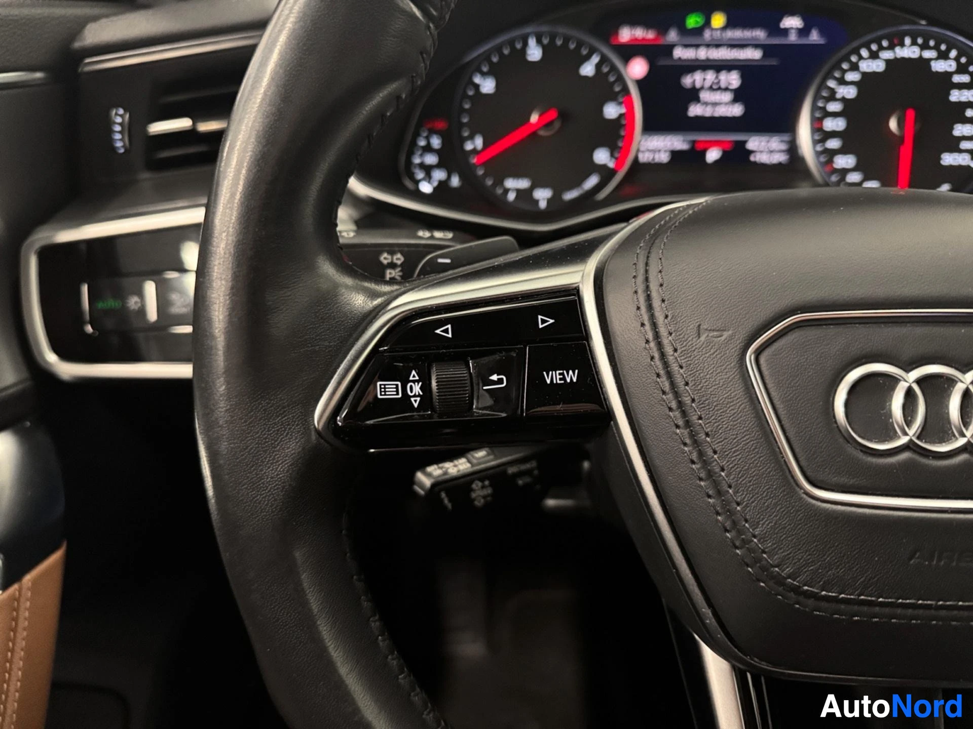 Steering wheel left side controls and paddle shifters, brown leather seat visible