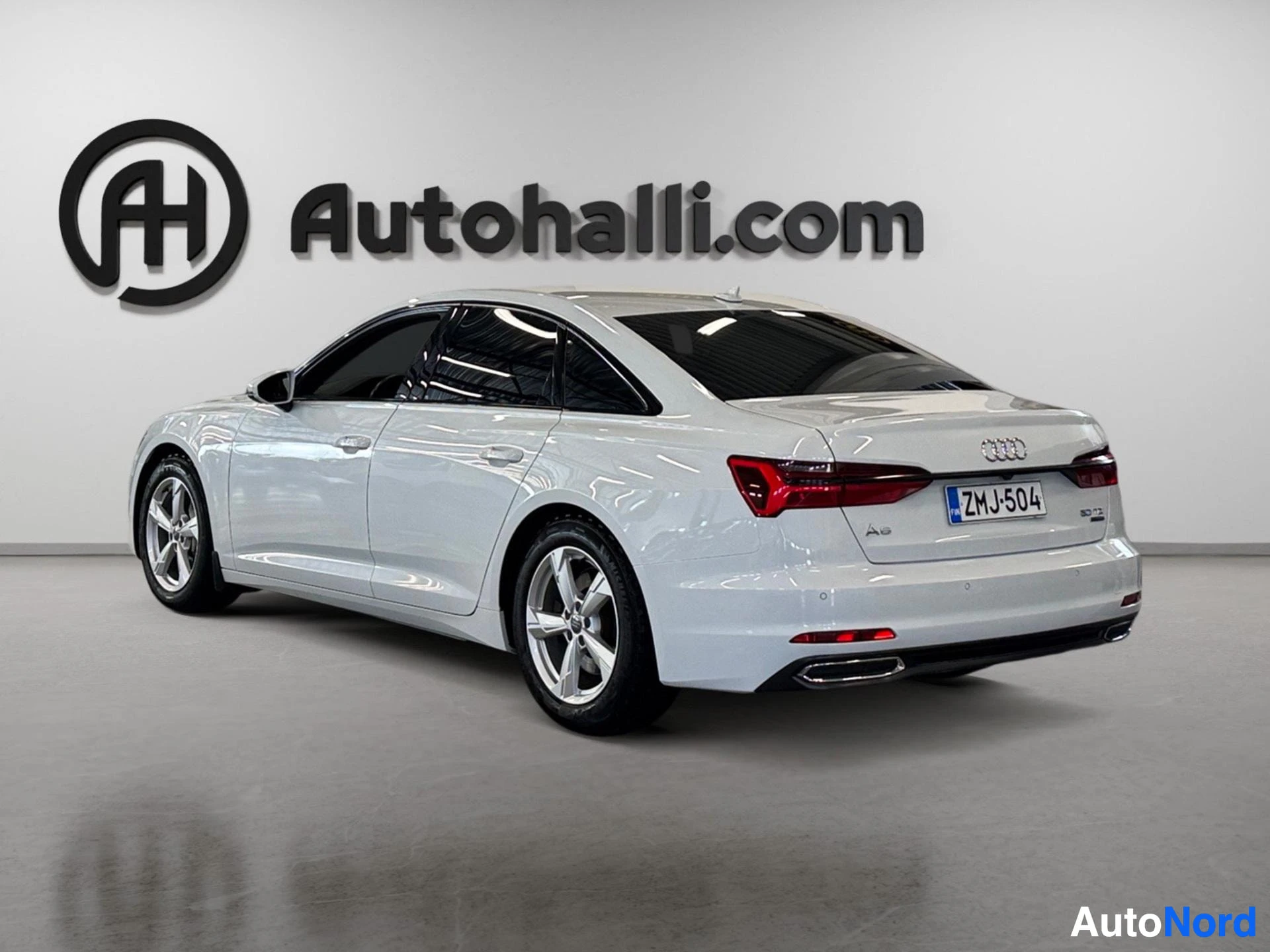 Valkoinen Audi A6 sedan takaa sivusta kuvattuna, kokonaisuus näkyvissä