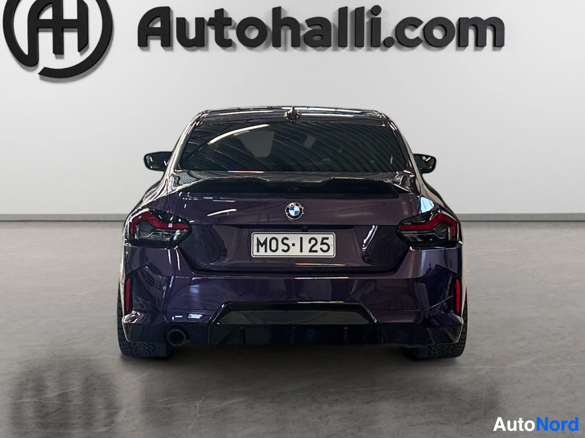 Dark purple BMW coupe viewed from rear, parked indoors against white wall
