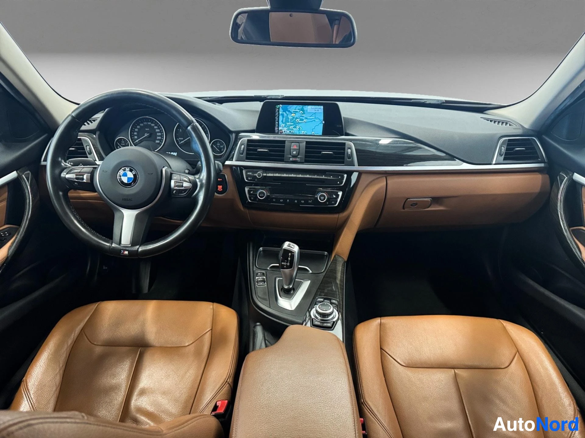 Ohjaamon etunäkymä: BMW-logo, ruskeat nahkaistuimet, kosketusnäyttö