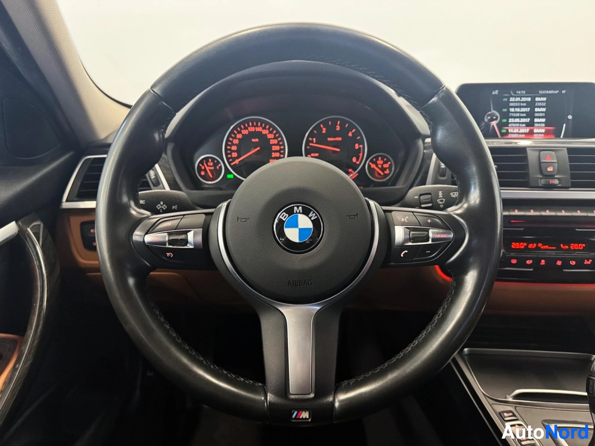 BMW-merkillä varustettu ohjauspyörä ja mittaristo punaisilla neuleilla