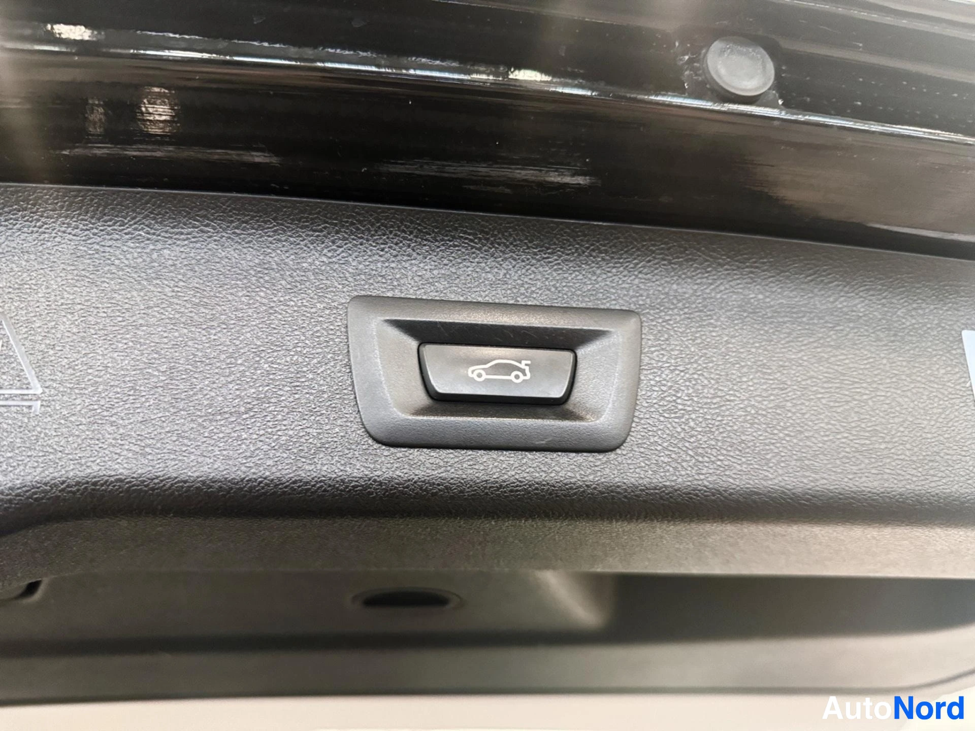 Trunk release button with car icon on gray interior trim panel