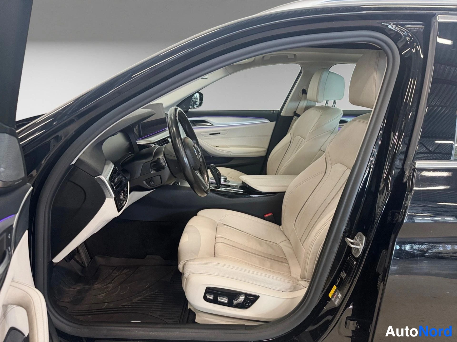 Beige leather interior with steering wheel, dashboard, and cream front seats in open driver door