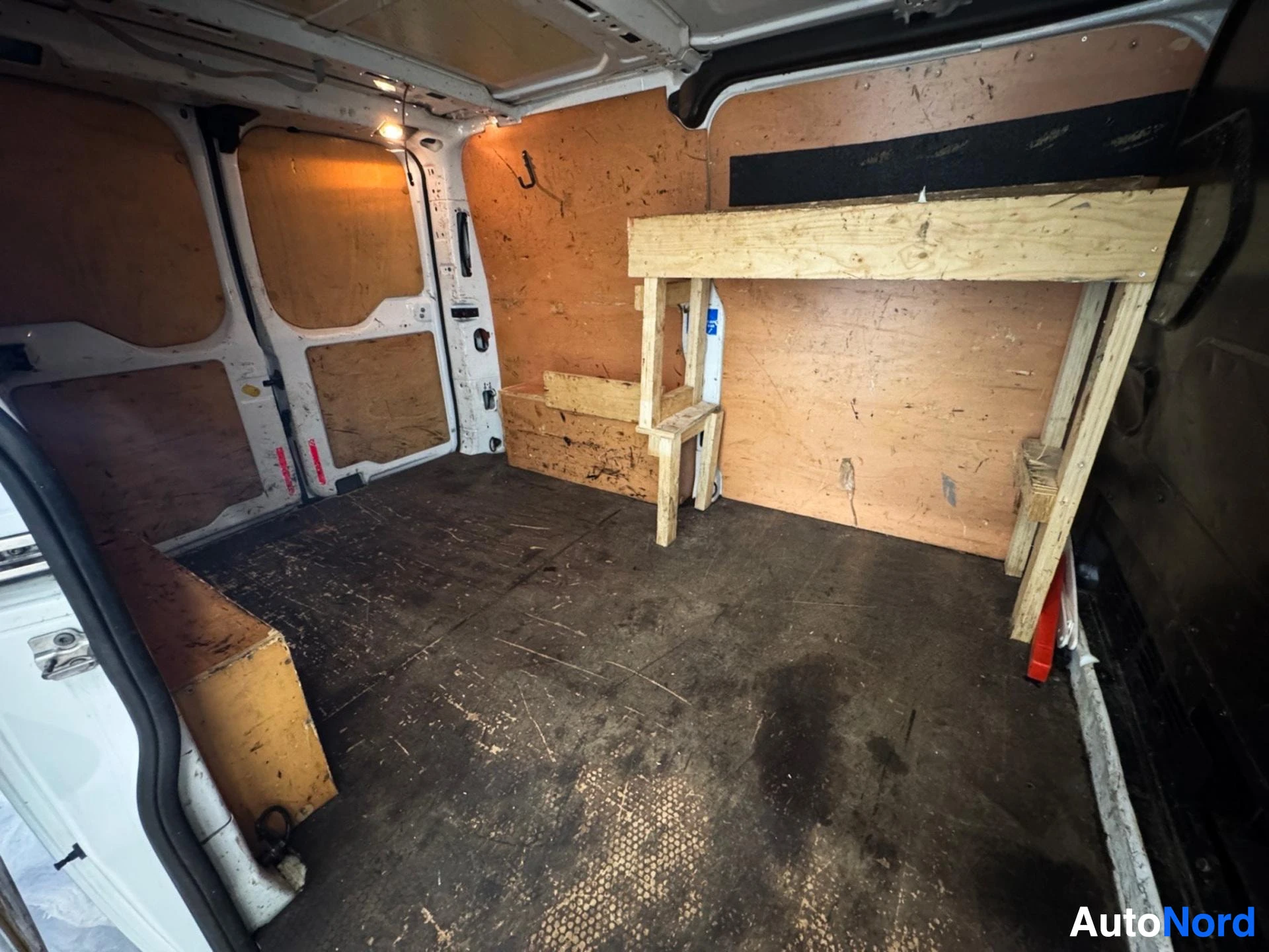 Van cargo interior with wooden shelving unit, plywood panels covering windows and walls