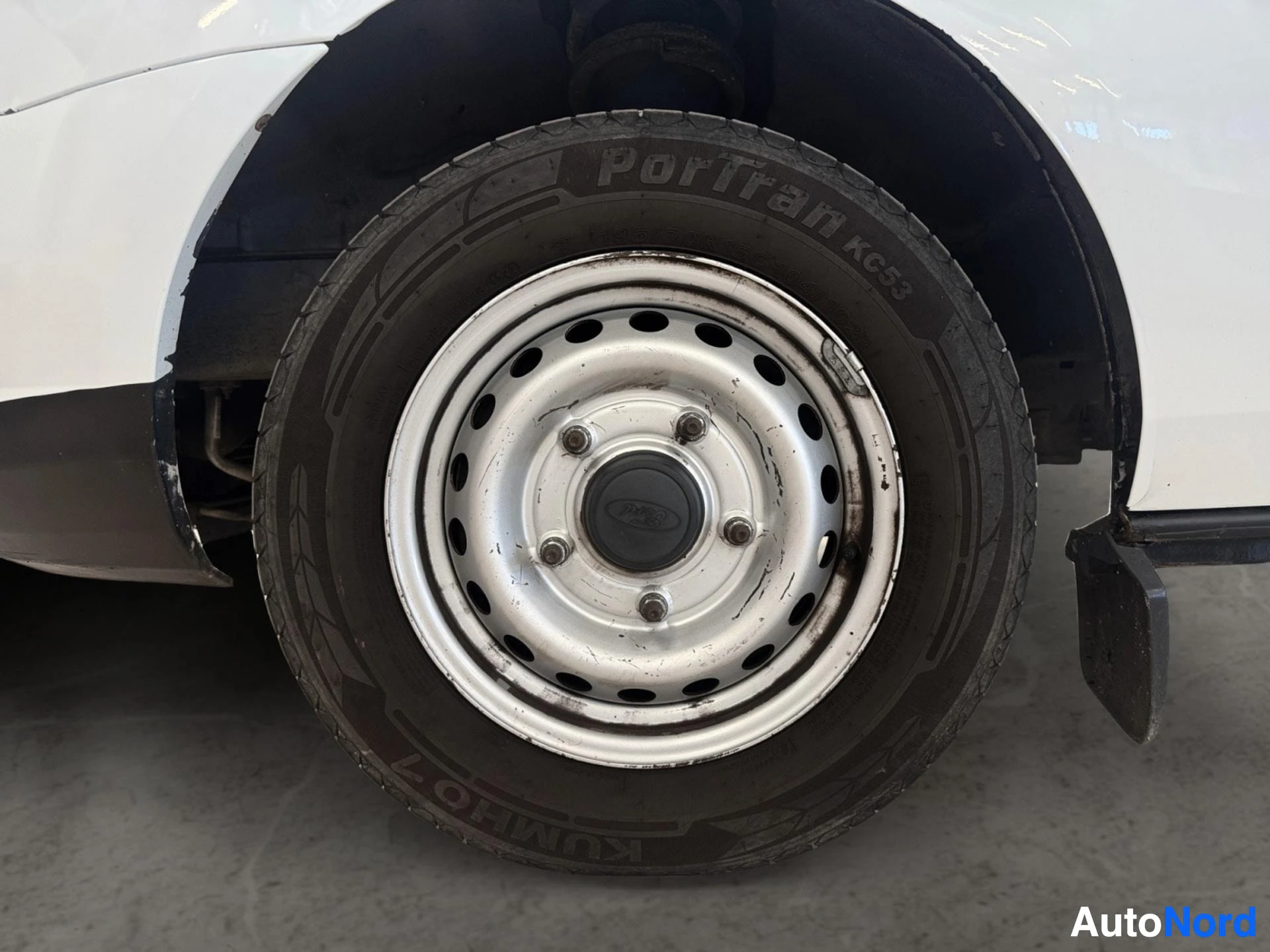 White van wheel with Portage tire and metal-centered hubcap showing wear marks