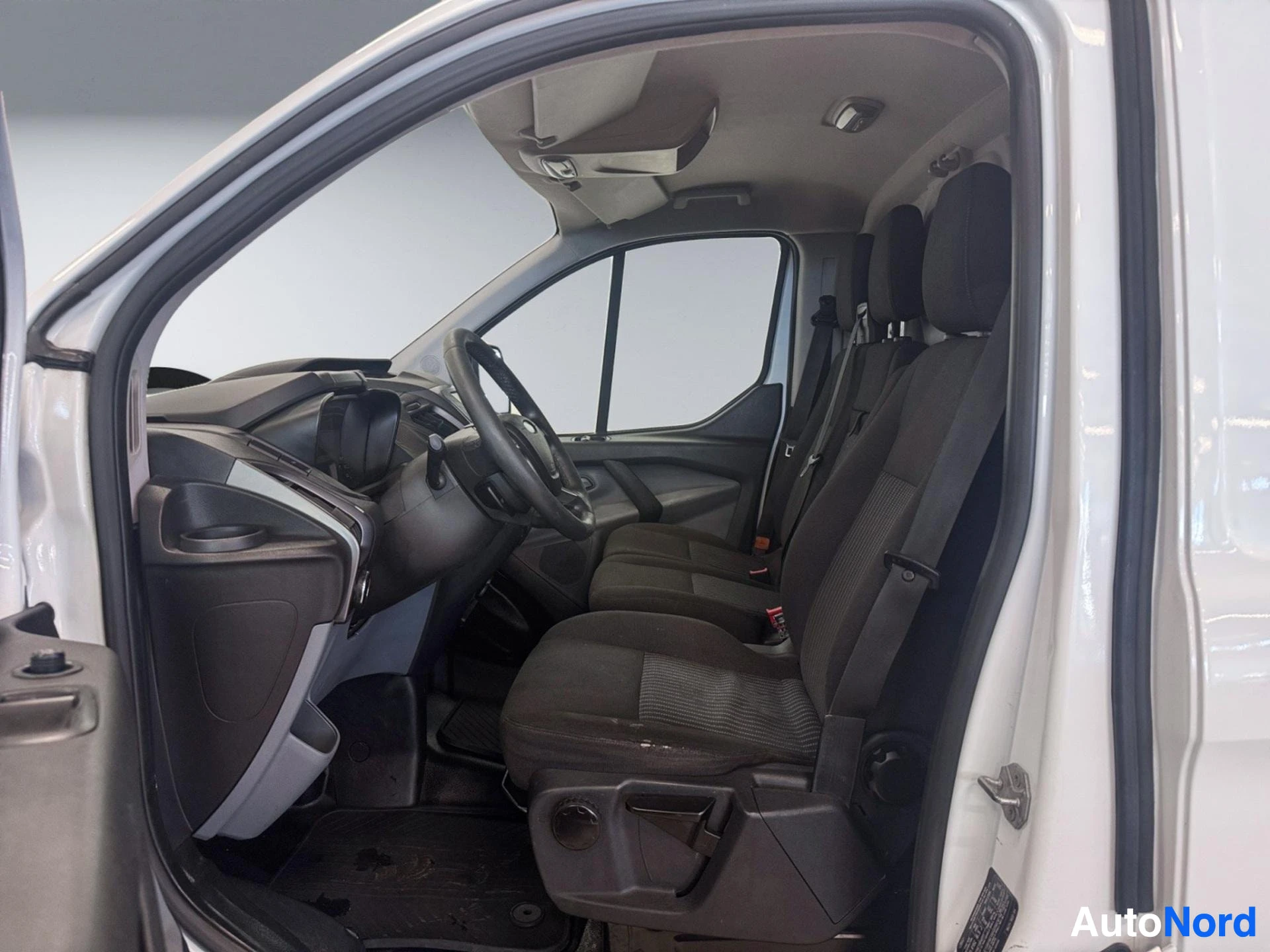 Van interior showing steering wheel, dashboard, black fabric seats and windshield