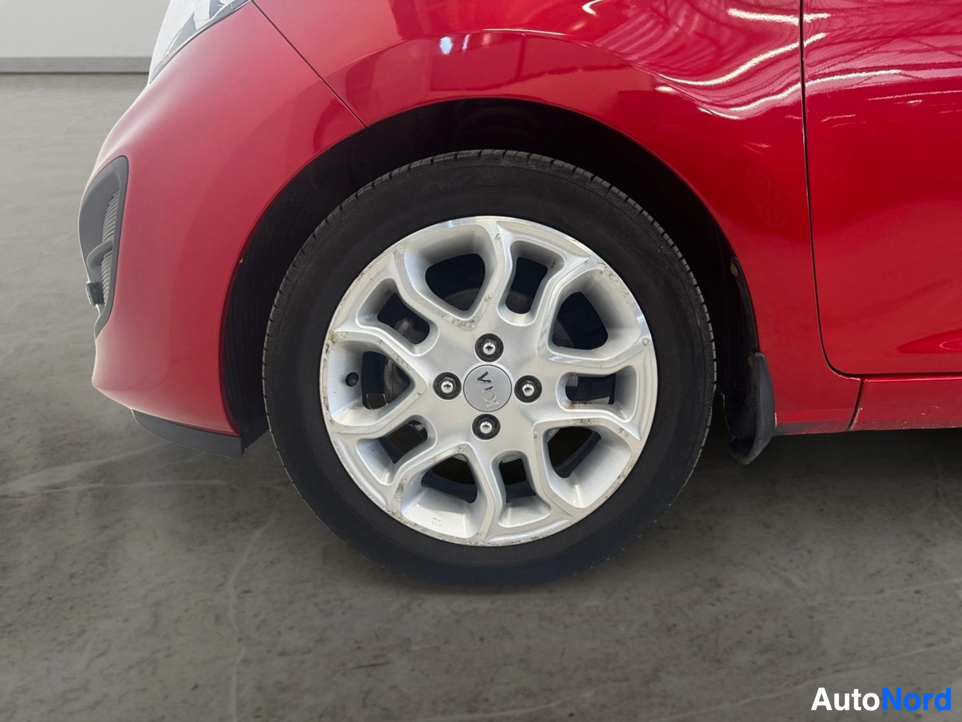 Front wheel with white alloy rim and black tire on red car body