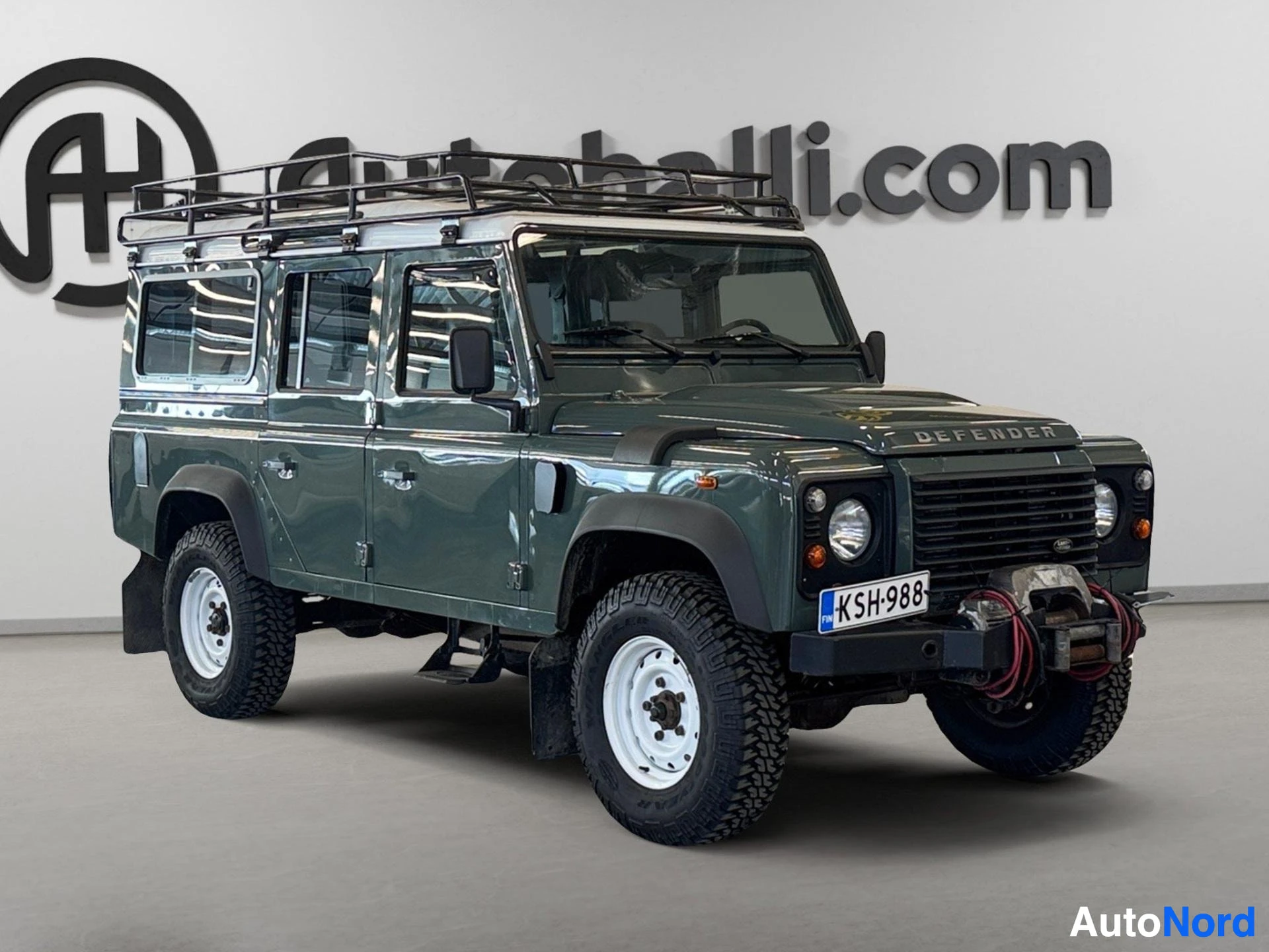 Vihreä Land Rover Defender 110 SW sivusta kulmasta, roofframe ja accesories.