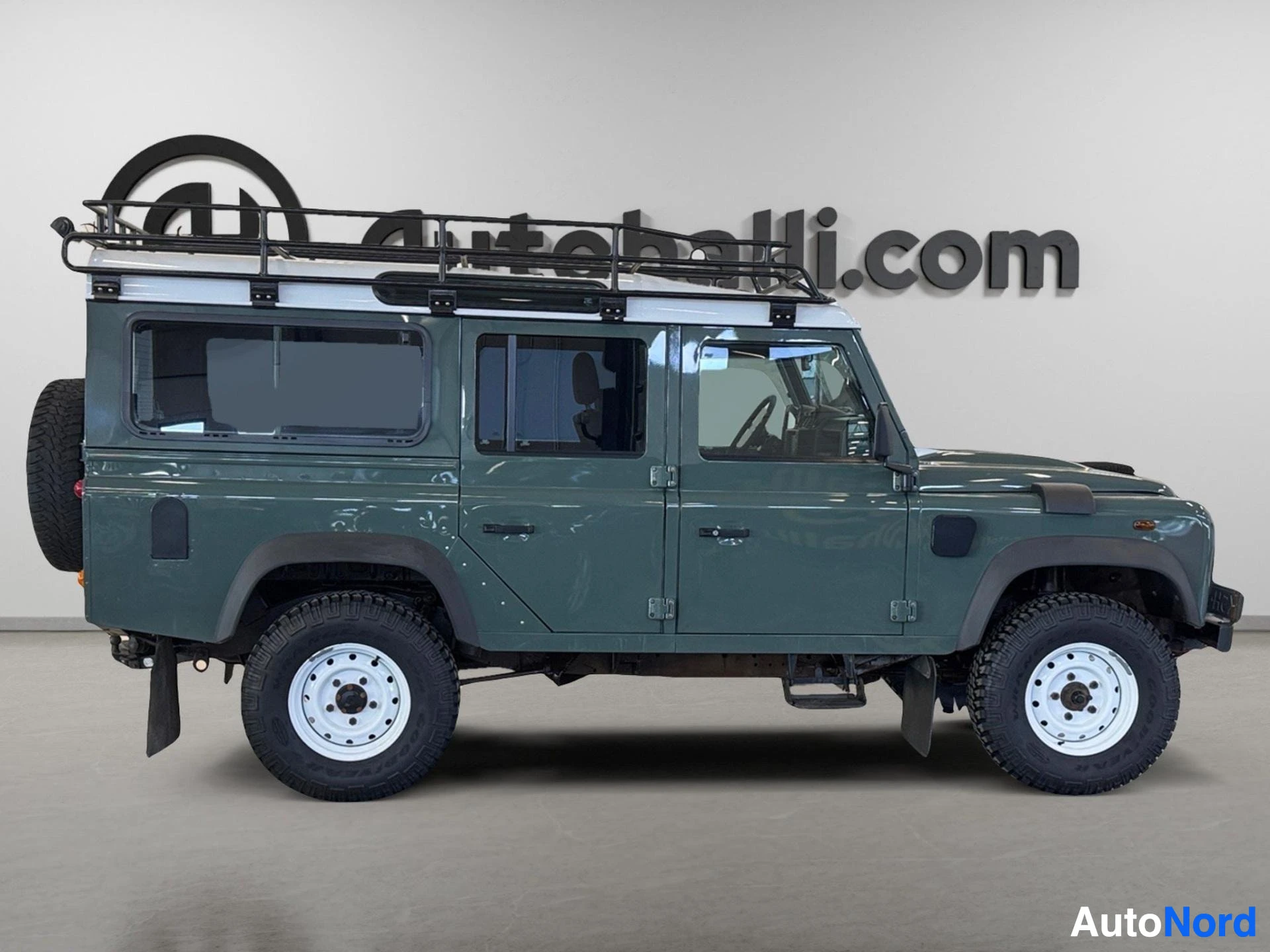 Vihreä Land Rover Defender 110 SW suoraan sivusta, roof frame ja varusteet.