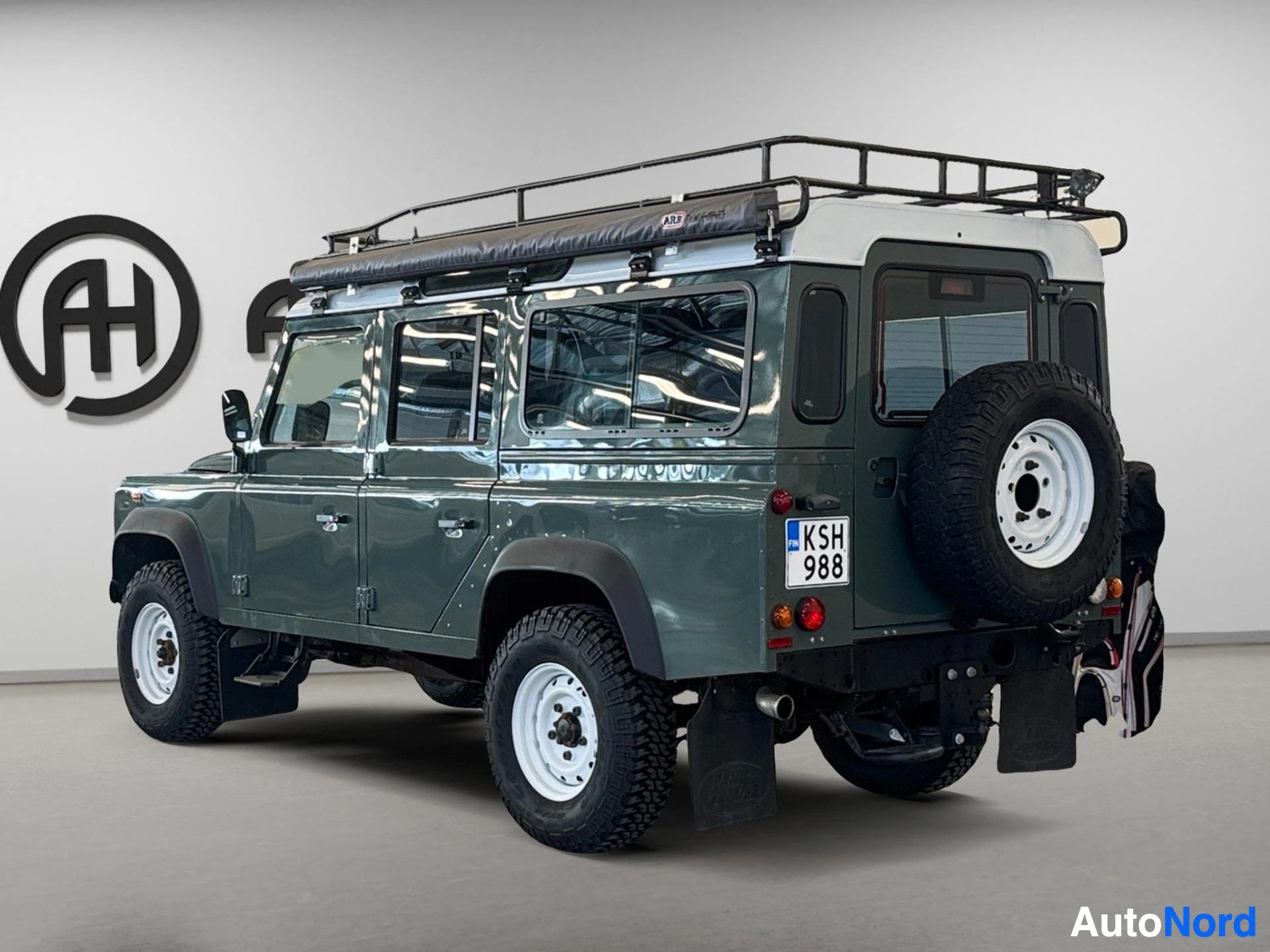 Vihreä Land Rover Defender 110 SW takaa oikealta, kattotelineella ja säilytysrenkaalla