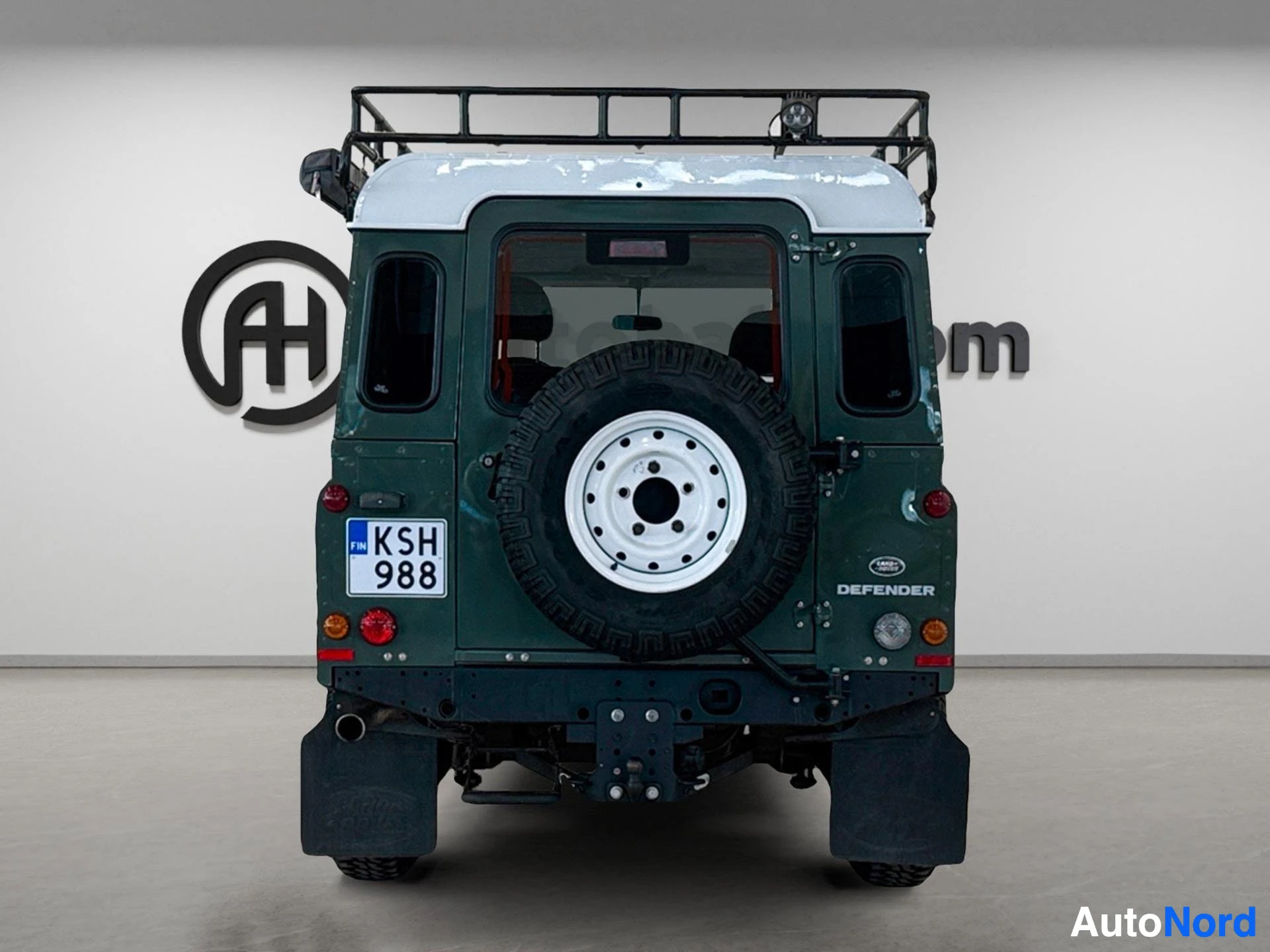 Vihreä Land Rover Defender 110 SW suoraan takaa, säilytysrenkaalla ja kattotelineella