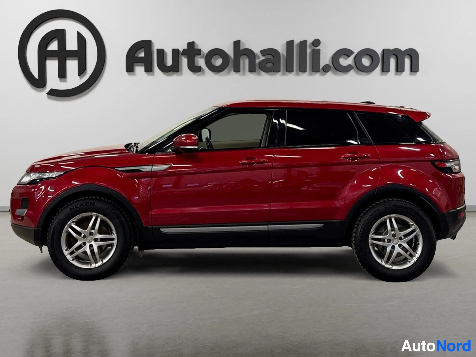 Punainen Range Rover Evoque kuvan sivusta, valkoiset vanteet ja tummennnetut ikkunat