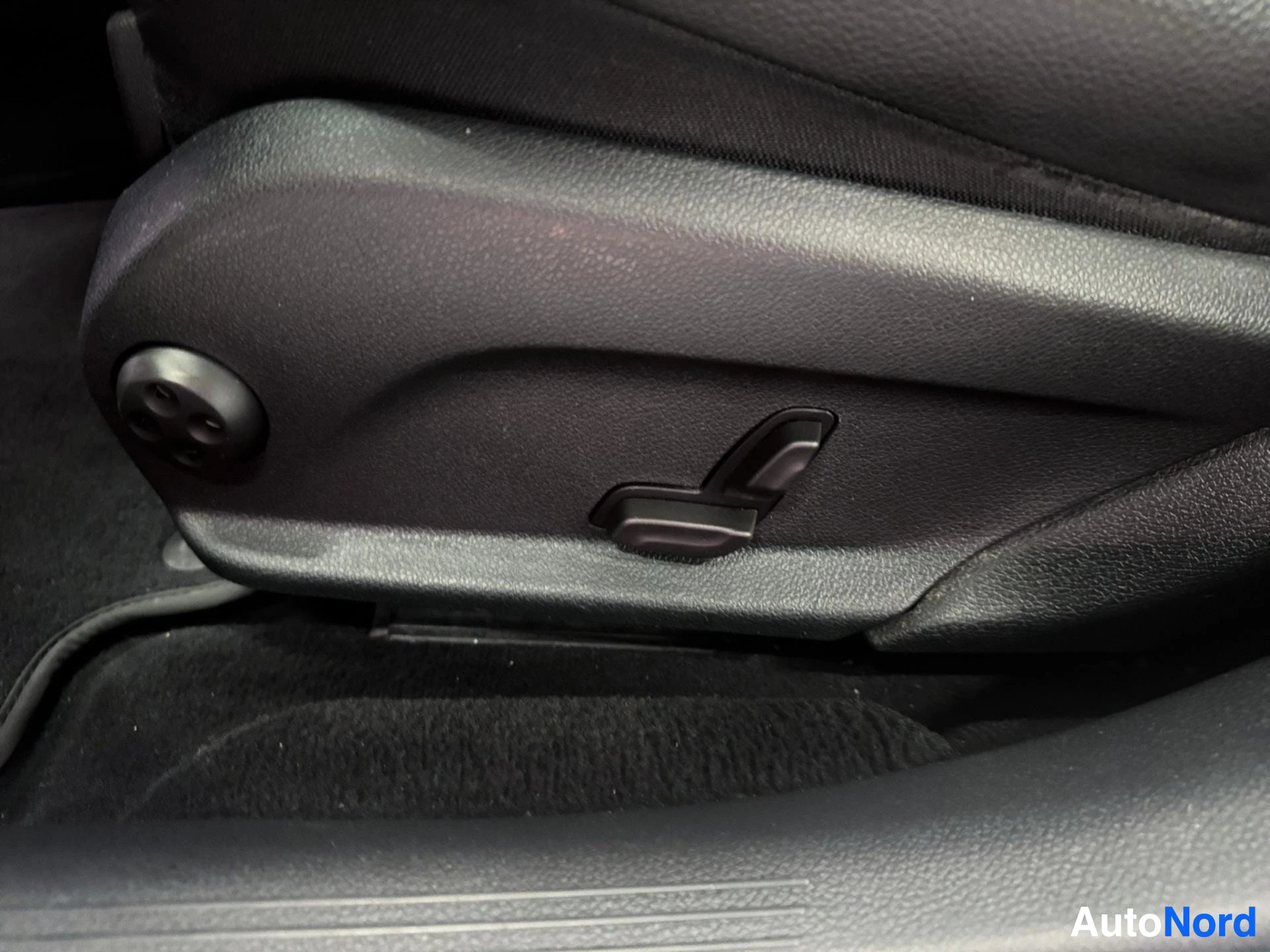 Close-up of black leather seat armrest with adjustment controls and stitching detail.