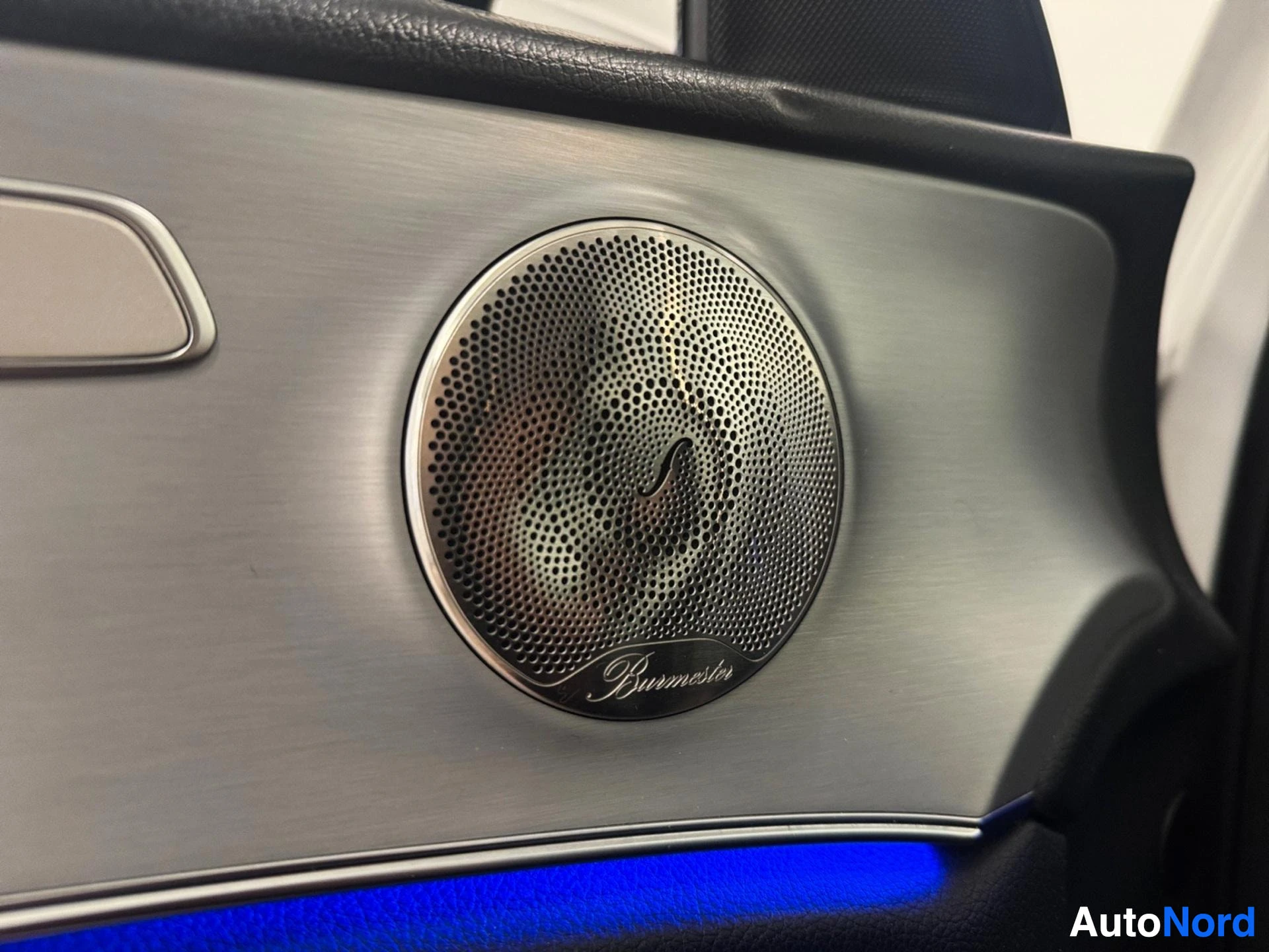 Door panel speaker with Burmester branding and metallic trim with blue ambient lighting.