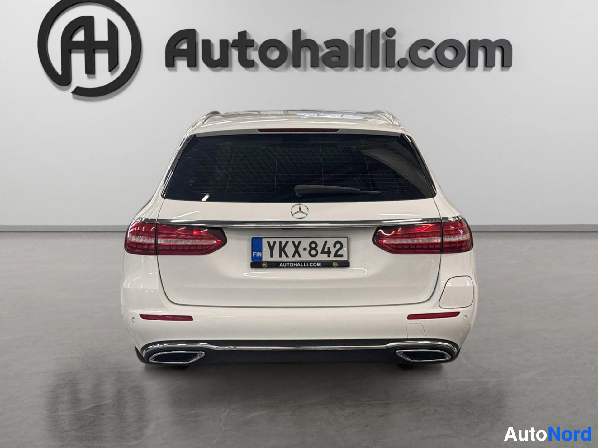 White Mercedes-Benz sedan rear view with red LED taillights and dual exhaust pipes.