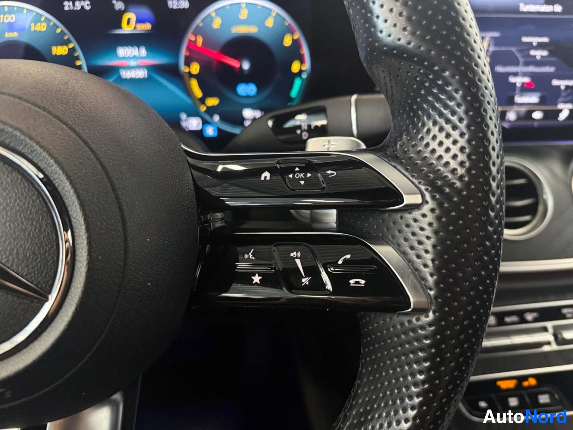 Perforated leather steering wheel with control buttons and instrument gauges behind