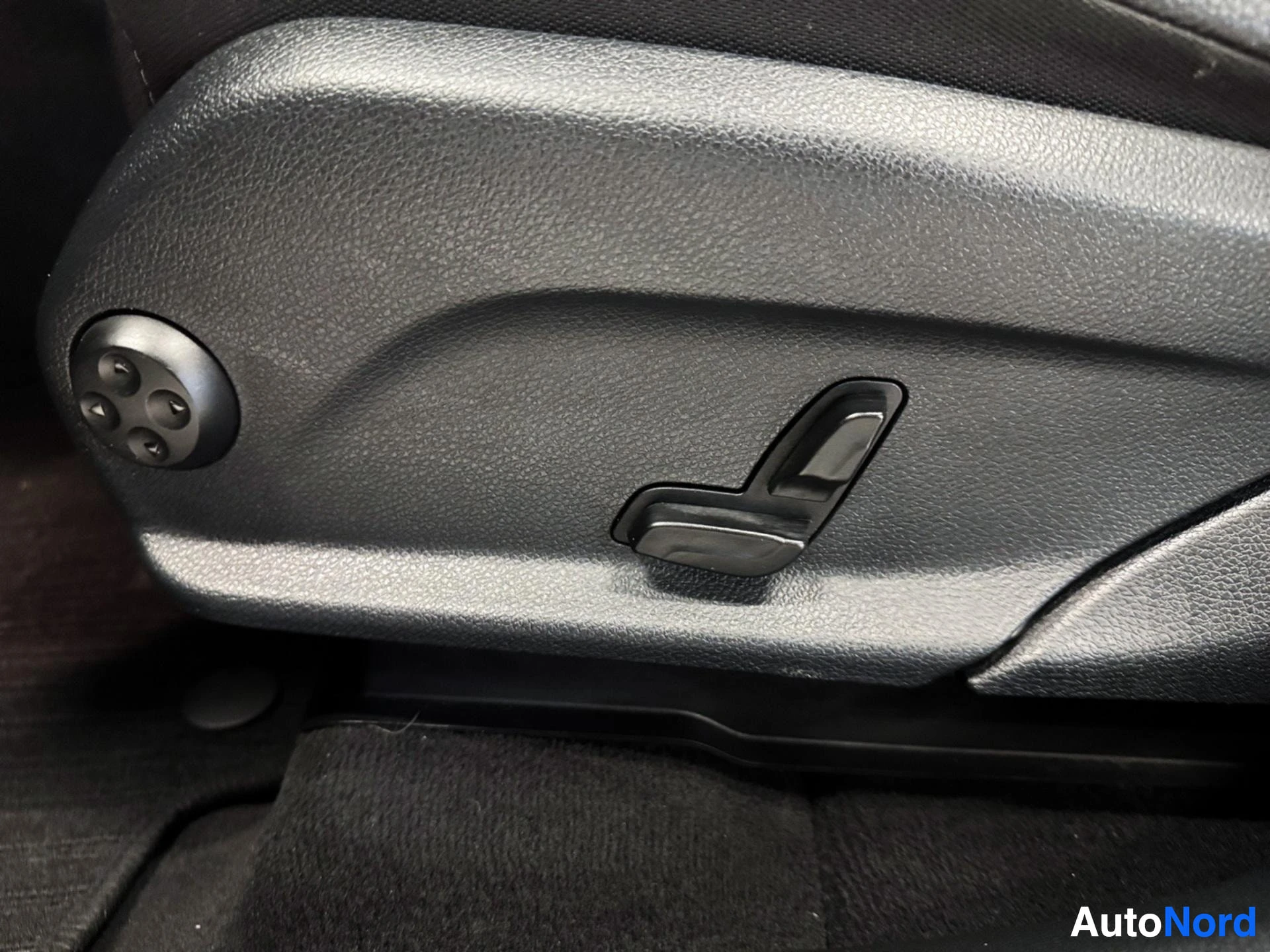 Driver seat adjustment controls with memory button and fabric material.