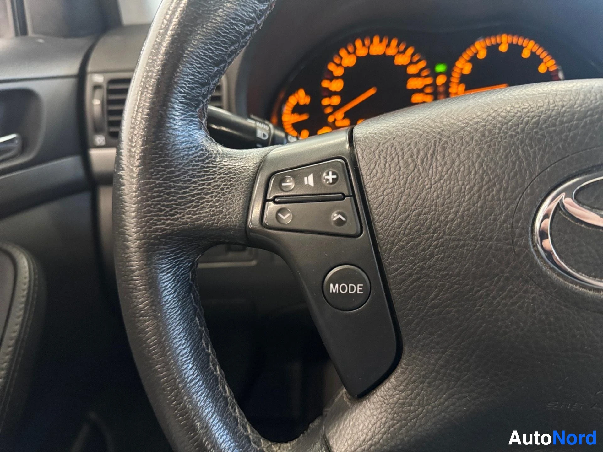 Steering wheel with leather grip and control buttons, orange dashboard gauges visible