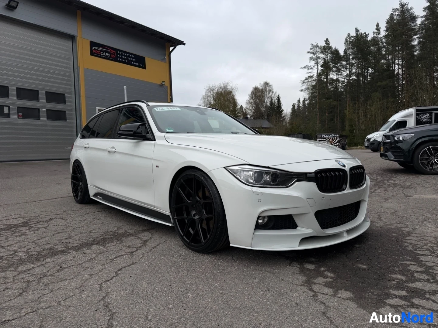 White BMW estate car front three-quarter view, black wheels, dealer lot