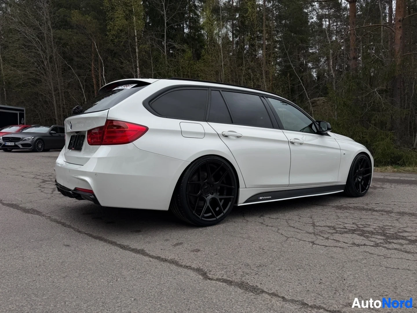 White BMW estate car rear side profile against forest backdrop
