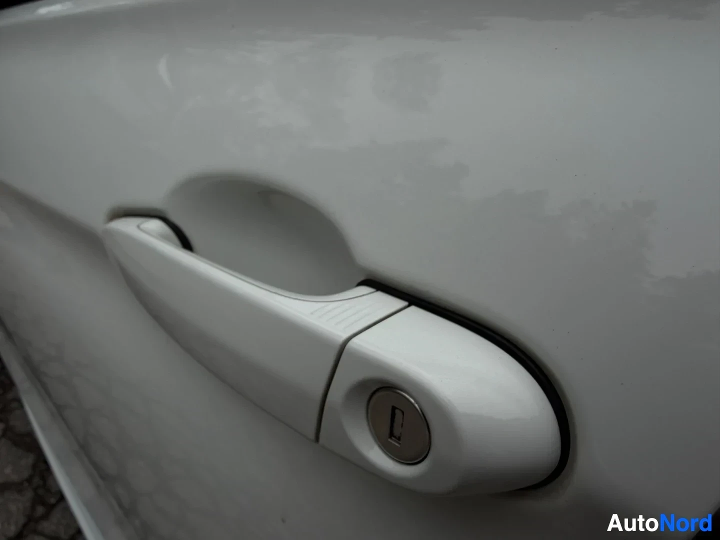 White door handle with lock cylinder on vehicle exterior.