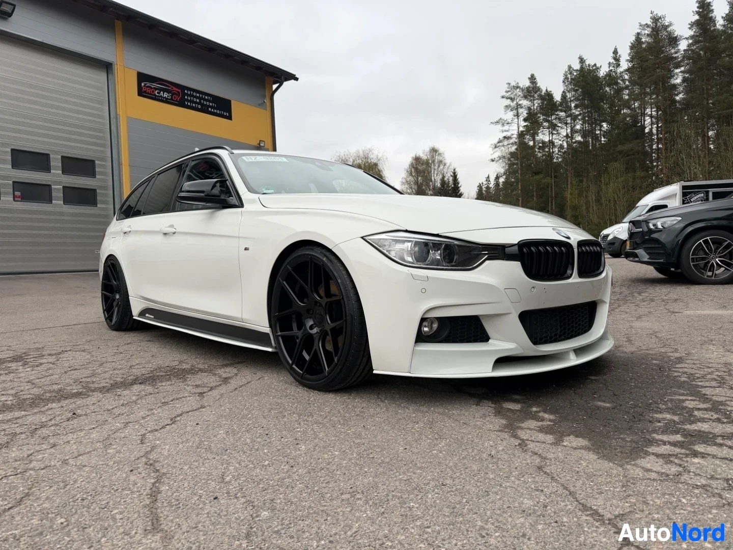 White BMW estate car front side view, black wheels, dealer building