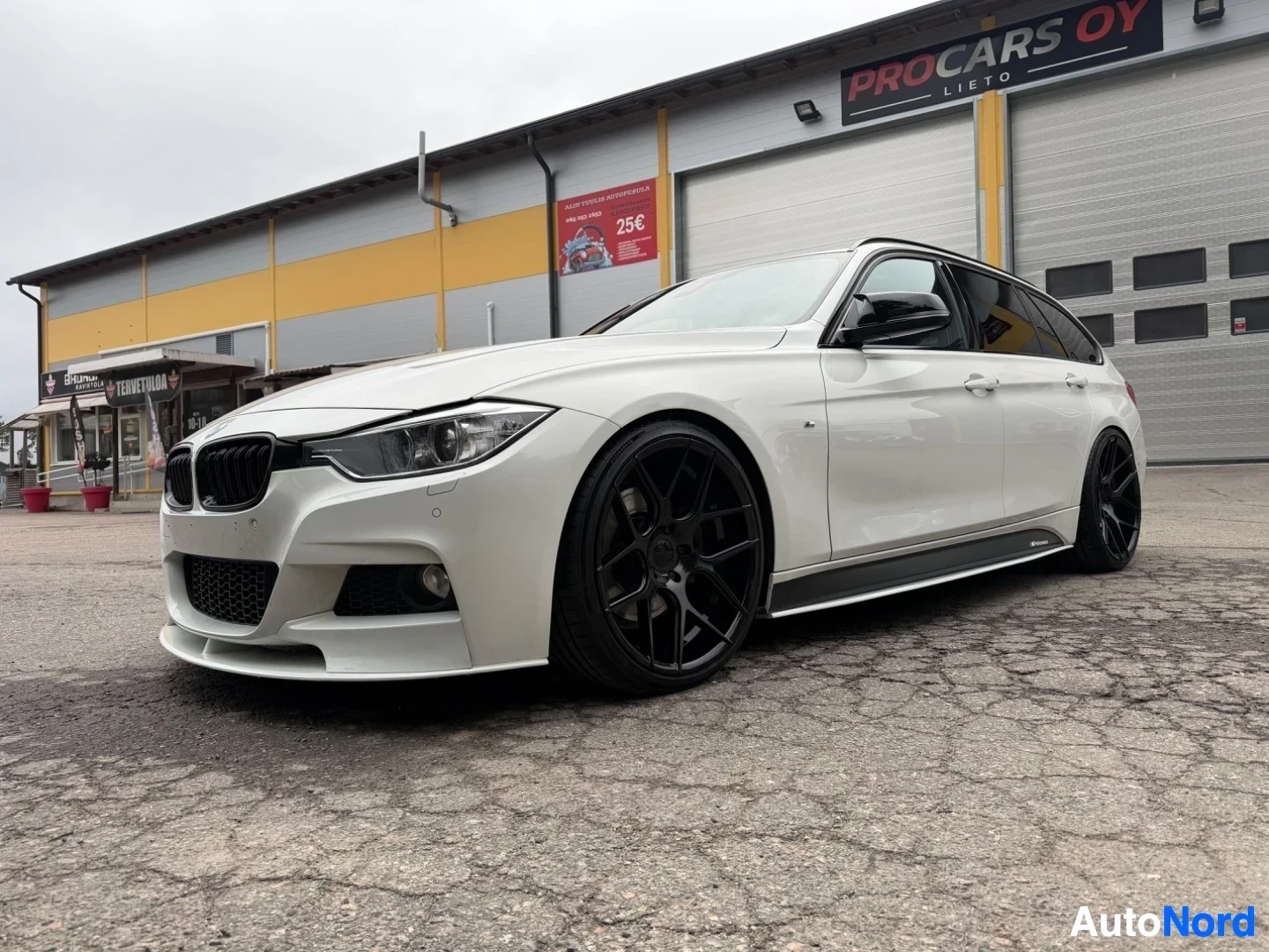 Valkoinen BMW farmari sivusta kuvattu, mustat vanteet, autokaupan piha-alueella