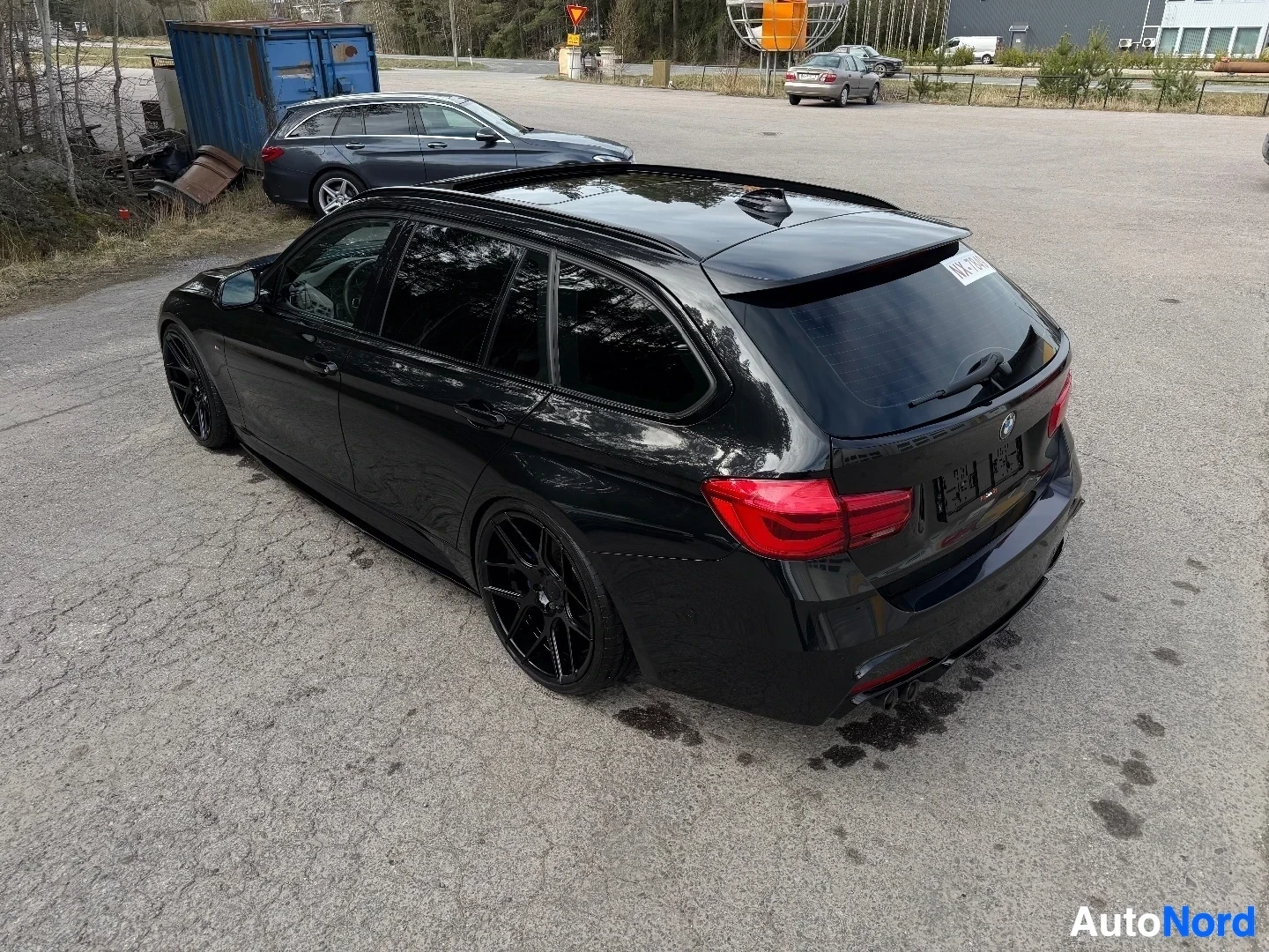 Musta BMW farmari näkyy takavasemmalta kulmalta paikoitusalueella.