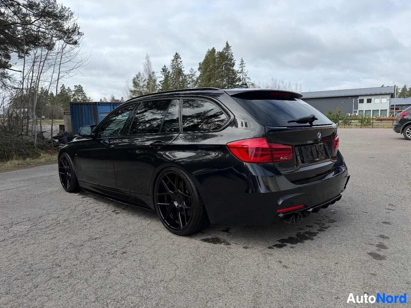 Musta BMW farmari näkyy takaa oikealta kulmalta metsän lähellä.